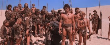 Movie still from “Mad Max Beyond Thunderdome” (1985), directed by George Miller – A group of young men standing on top of a sandy beach; Wide shot, High angle