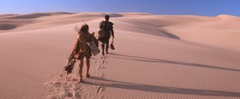 Movie still from “Mad Max Beyond Thunderdome” (1985), directed by George Miller – A man and a woman walking through the sand dunes; Wide shot, High angle
