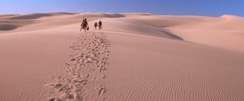 Movie still from “Mad Max Beyond Thunderdome” (1985), directed by George Miller – A group of people walking across a sand dune; Extreme Wide shot, High angle