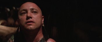Movie still from “Mad Max Beyond Thunderdome” (1985), directed by George Miller – A bald man with long black hair and a piercing; Close Up shot, Low angle