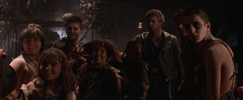 Movie still from “Mad Max Beyond Thunderdome” (1985), directed by George Miller – A group of people standing next to each other in a room; Medium shot, Low angle