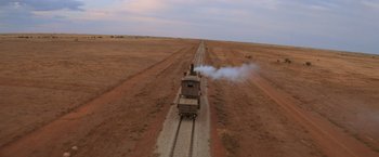 Movie still from “Mad Max Beyond Thunderdome” (1985), directed by George Miller – An aerial view of a train on the tracks in the middle of the desert; Extreme Wide shot, High angle