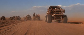 Movie still from “Mad Max Beyond Thunderdome” (1985), directed by George Miller – A group of people riding on the back of a four wheeler; Wide shot, Low angle