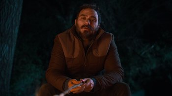 Movie still from “Mae Martin: SAP” (2023), directed by Abbi Jacobson – A man sitting in the dark holding a fishing pole; Medium shot, Low angle