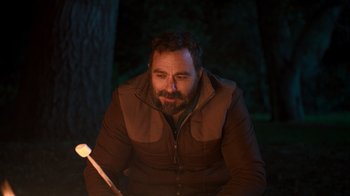 Movie still from “Mae Martin: SAP” (2023), directed by Abbi Jacobson – A man sitting in the dark holding a stick; Medium shot, Over the shoulder angle