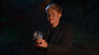 Movie still from “Mae Martin: SAP” (2023), directed by Abbi Jacobson – A man holding a crystal ball in a dark forest; Close Up shot, Over the shoulder angle