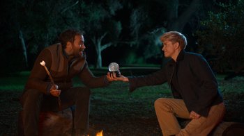 Movie still from “Mae Martin: SAP” (2023), directed by Abbi Jacobson – Two men are holding hands around a campfire; Medium shot, Over the shoulder angle