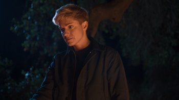 Movie still from “Mae Martin: SAP” (2023), directed by Abbi Jacobson – A man with blonde hair standing in the dark; Close Up shot, Over the shoulder angle