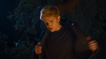 Movie still from “Mae Martin: SAP” (2023), directed by Abbi Jacobson – A man in a black shirt is holding a knife; Medium shot, Over the shoulder angle