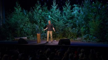 Movie still from “Mae Martin: SAP” (2023), directed by Abbi Jacobson – A man standing on a stage in front of a crowd; Wide shot, High angle