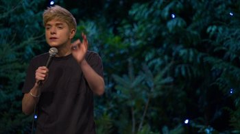 Movie still from “Mae Martin: SAP” (2023), directed by Abbi Jacobson – A young man standing in front of a tree; Close Up shot, Over the shoulder angle