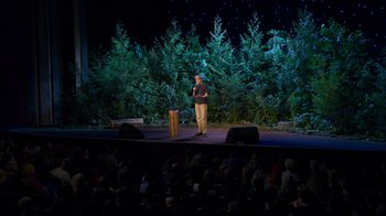 Movie still from “Mae Martin: SAP” (2023), directed by Abbi Jacobson – A man standing on a stage in front of an audience; Extreme Wide shot, High angle