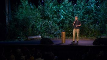 Movie still from “Mae Martin: SAP” (2023), directed by Abbi Jacobson – A man standing on a stage in front of a crowd; Wide shot, High angle