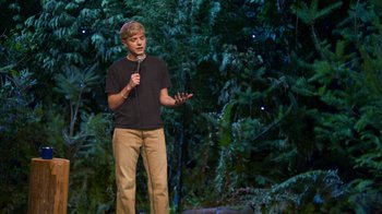 Movie still from “Mae Martin: SAP” (2023), directed by Abbi Jacobson – A man standing on a stage holding a microphone; Wide shot, High angle