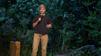 Movie still from “Mae Martin: SAP” (2023), directed by Abbi Jacobson – A man standing on a stage holding a microphone; Wide shot, High angle