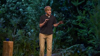 Movie still from “Mae Martin: SAP” (2023), directed by Abbi Jacobson – A man standing on a stage holding a microphone; Wide shot, High angle