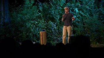 Movie still from “Mae Martin: SAP” (2023), directed by Abbi Jacobson – A man standing on a stage in front of a crowd; Wide shot, High angle