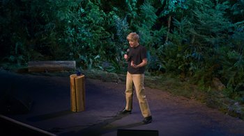 Movie still from “Mae Martin: SAP” (2023), directed by Abbi Jacobson – A man standing on a stage holding a microphone; Wide shot, High angle