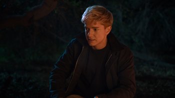 Movie still from “Mae Martin: SAP” (2023), directed by Abbi Jacobson – A man sitting in the dark in front of a tree; Close Up shot, Over the shoulder angle