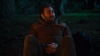 Movie still from “Mae Martin: SAP” (2023), directed by Abbi Jacobson – A man sitting on the ground at night in the dark; Medium shot, Over the shoulder angle