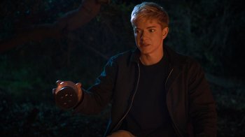 Movie still from “Mae Martin: SAP” (2023), directed by Abbi Jacobson – A man holding a bottle in his hand in the dark; Medium shot, Over the shoulder angle