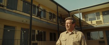 Movie still from “Maggie Moore(s)” (2023), directed by John Slattery – A man standing in front of an apartment building; Wide shot, Low angle