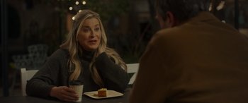 Movie still from “Maggie Moore(s)” (2023), directed by John Slattery – A woman sitting at a table with a plate of food; Medium shot, Over the shoulder angle