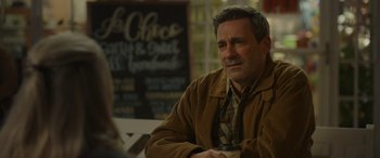 Movie still from “Maggie Moore(s)” (2023), directed by John Slattery – A man sitting at a table holding a coffee mug; Medium shot, Over the shoulder angle