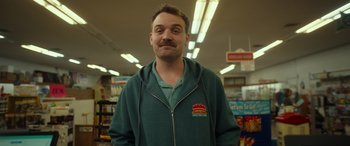 Movie still from “Maggie Moore(s)” (2023), directed by John Slattery – A man with a mustache standing inside of a store; Close Up shot, Low angle