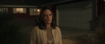 Movie still from “Maggie Moore(s)” (2023), directed by John Slattery – A woman standing in a dark room with her head turned to the side; Medium shot, Over the shoulder angle