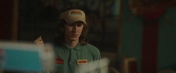 Movie still from “Maggie Moore(s)” (2023), directed by John Slattery – A man wearing a hat and a green polo shirt; Close Up shot, Over the shoulder angle