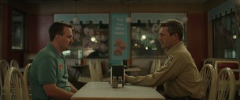 Movie still from “Maggie Moore(s)” (2023), directed by John Slattery – Two men sitting at a table in a restaurant; Medium shot, Over the shoulder angle