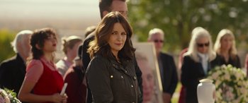 Movie still from “Maggie Moore(s)” (2023), directed by John Slattery – A woman standing in front of a group of people; Close Up shot, Over the shoulder angle