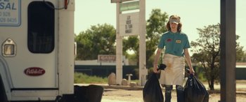 Movie still from “Maggie Moore(s)” (2023), directed by John Slattery – A woman carrying a bag of garbage while walking down the street; Medium shot, Low angle