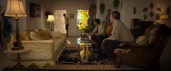 Movie still from “Maggie Moore(s)” (2023), directed by John Slattery – A group of men sitting around a living room together; Wide shot, Over the shoulder angle