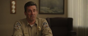 Movie still from “Maggie Moore(s)” (2023), directed by John Slattery – A police officer sitting at a table in front of a painting; Close Up shot, Over the shoulder angle