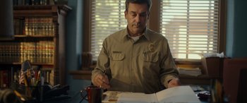 Movie still from “Maggie Moore(s)” (2023), directed by John Slattery – A man sitting at a table writing on a piece of paper; Medium shot, Over the shoulder angle