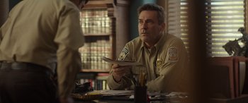 Movie still from “Maggie Moore(s)” (2023), directed by John Slattery – A man sitting at a table holding a piece of paper; Close Up shot, Over the shoulder angle