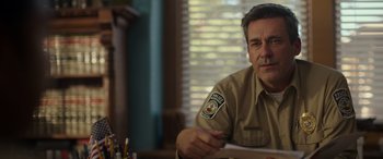 Movie still from “Maggie Moore(s)” (2023), directed by John Slattery – A man sitting at a table holding a paper; Close Up shot, Over the shoulder angle