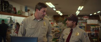 Movie still from “Maggie Moore(s)” (2023), directed by John Slattery – A man and a man in uniform talking to each other in a store; Medium shot, Over the shoulder angle