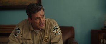 Movie still from “Maggie Moore(s)” (2023), directed by John Slattery – A police officer sitting in front of a blue wall; Close Up shot, Over the shoulder angle