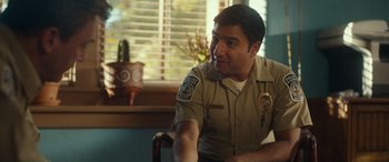 Movie still from “Maggie Moore(s)” (2023), directed by John Slattery – A cop sitting in a chair in front of a window; Medium shot, Over the shoulder angle