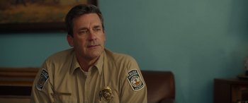 Movie still from “Maggie Moore(s)” (2023), directed by John Slattery – A police officer sitting in a chair with his hand on his chin; Close Up shot, Over the shoulder angle