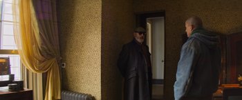 Movie still from “Magic Mike's Last Dance” (2023), directed by Steven Soderbergh – A man in a coat and hat standing next to a door; Medium shot, Low angle