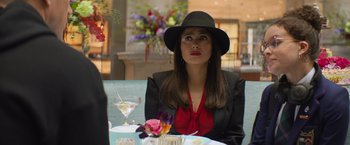 Movie still from “Magic Mike's Last Dance” (2023), directed by Steven Soderbergh – A woman sitting at a table with a black hat on; Medium shot, Over the shoulder angle