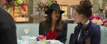 Movie still from “Magic Mike's Last Dance” (2023), directed by Steven Soderbergh – A woman wearing a black hat sitting at a table; Medium shot, Over the shoulder angle