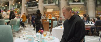 Movie still from “Magic Mike's Last Dance” (2023), directed by Steven Soderbergh – A man sitting at a table in front of a bunch of people; Medium shot, Over the shoulder angle