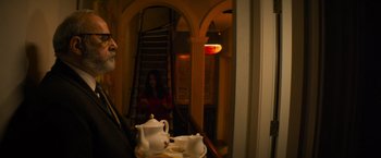 Movie still from “Magic Mike's Last Dance” (2023), directed by Steven Soderbergh – A man sitting in front of a table with a tea set; Medium shot, Over the shoulder angle