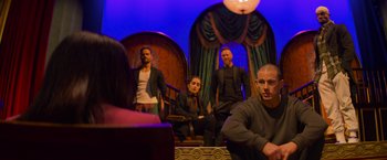 Movie still from “Magic Mike's Last Dance” (2023), directed by Steven Soderbergh – A group of people sitting in chairs in a room; Wide shot, Over the shoulder angle