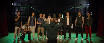 Movie still from “Magic Mike's Last Dance” (2023), directed by Steven Soderbergh – A group of young men standing in front of an instructor; Wide shot, High angle